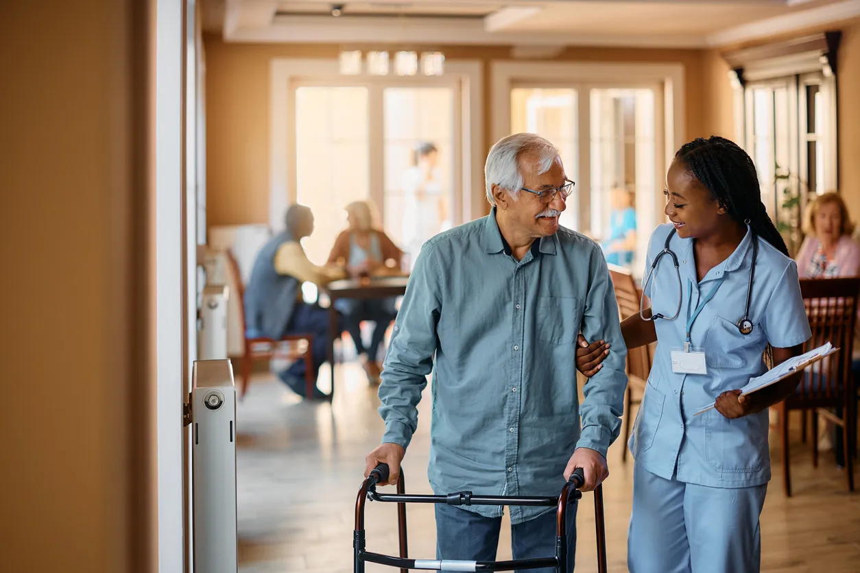Older man using a walker while a care team member walks beside him.