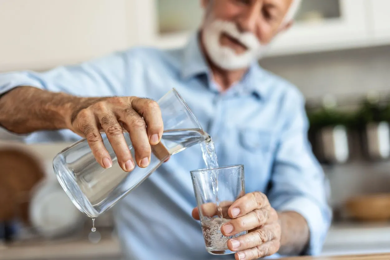 An older man pours a refreshing glass of water in his kitchen to hydrate himself.