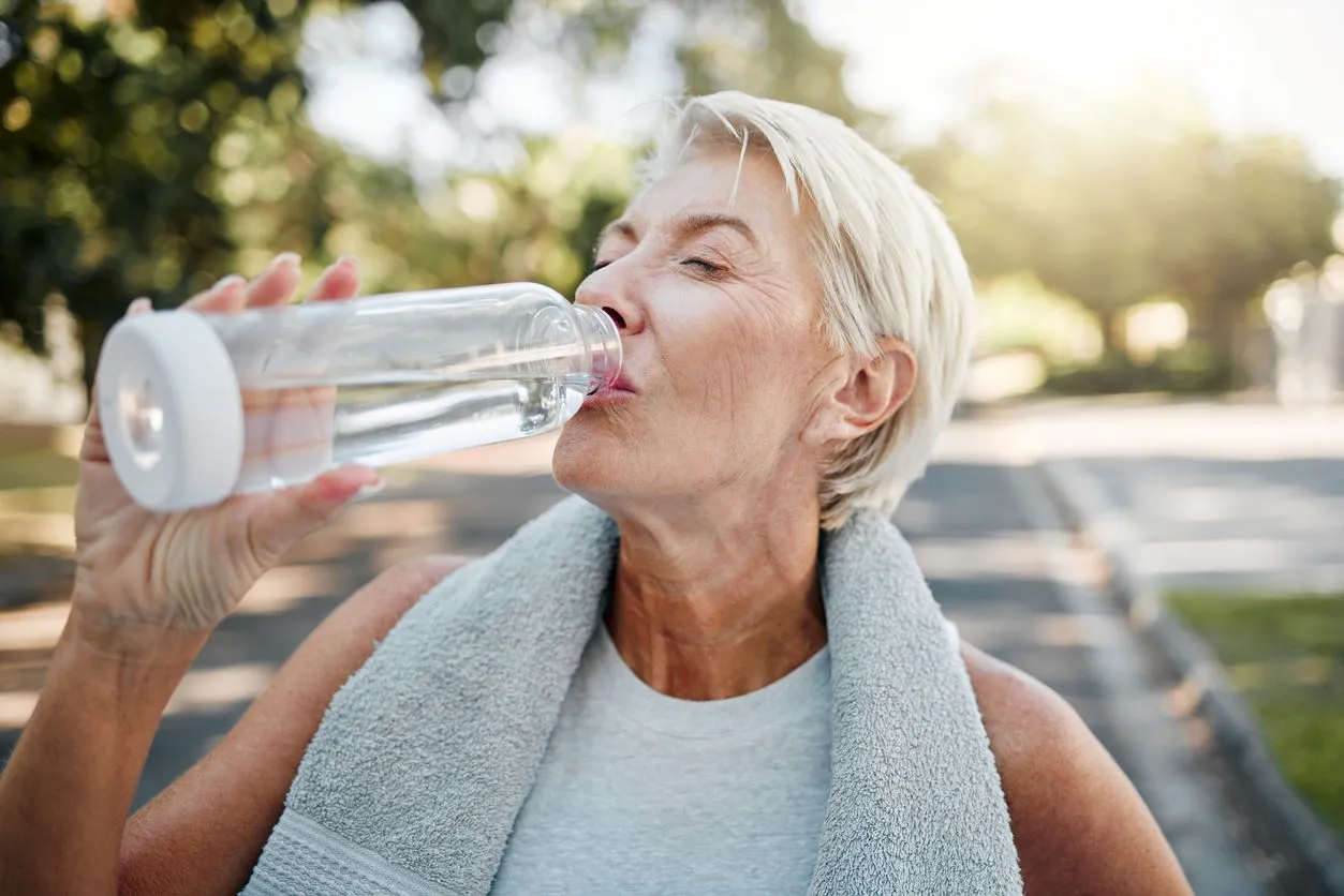 An older woman sips from a glass water bottle while exercising.