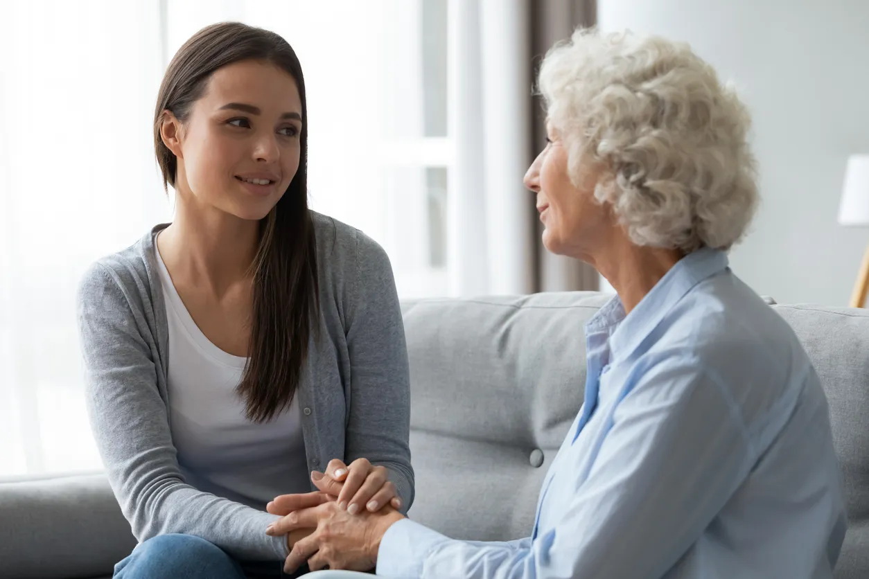 Younger woman holding an older woman's hands while they sit across from each other at a kitchen table