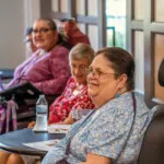 Show photo 87: A resident laughing with neighbors in the bistro