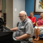 Show photo 85: A resident playing the piano for neighbors