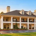 Show photo 1: The two-story white-columned porch at Tarina of Cypresswood with the flag out front at sunset